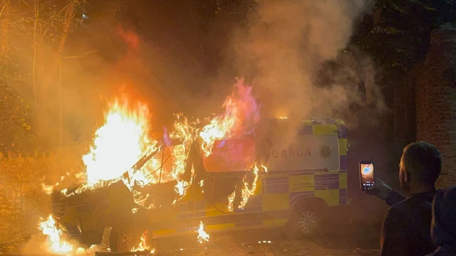Warga merekam sebuah kendaraan polisi yang terbakar saat demonstrasi di luar sebuah hotel tempat para pencari suaka bergejolak di Saggart, barat daya Dublin, Irlandia, Selasa (21/10/2025). Foto: PETER MURPHY/AFP