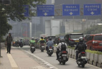 Seorang pekerja berjalan dengan mengenakan masker didekat kendaraan bermotor yang melintas di Jalan Sudirman, Jakarta, Kamis (26/6/2025). Foto: Jamal Ramadhan/kumparan